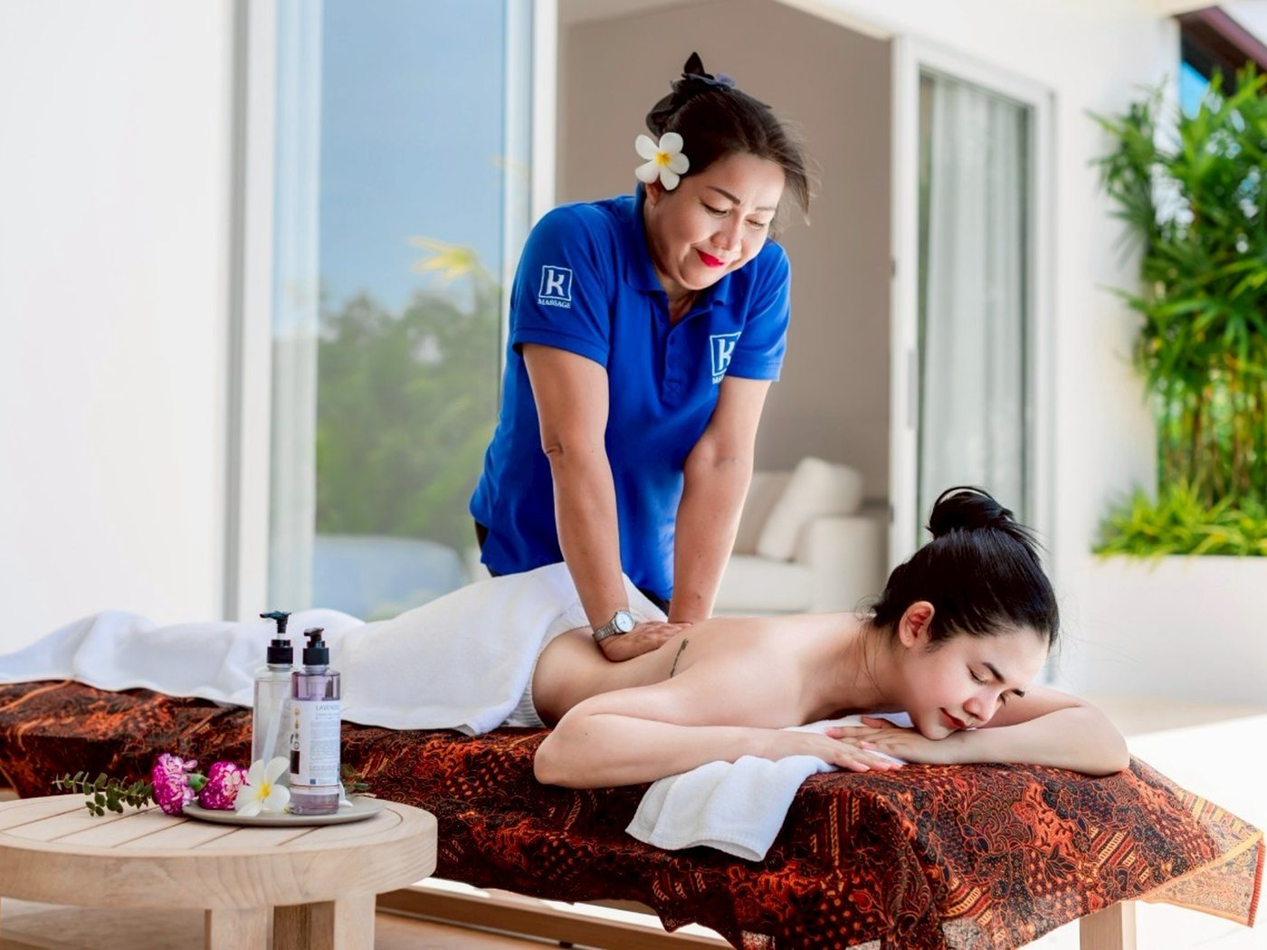 A therapist giving a massage on a daybed beside a private villa pool